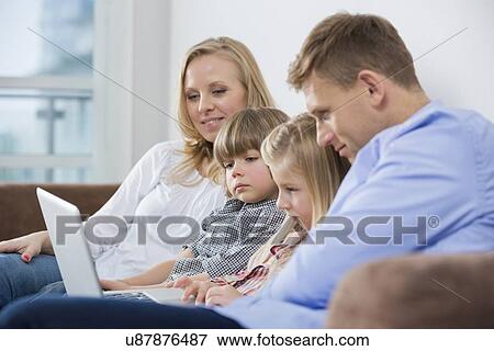 Parents with children using laptop on sofa at home View Large Photo Image Stock Photo - Parents with children using laptop on sofa at home. Fotosearch