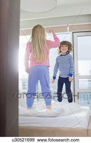 Playful brother and sister standing on bed View Large Photo Image Stock Photo - Playful brother and sister standing on bed. Fotosearch
