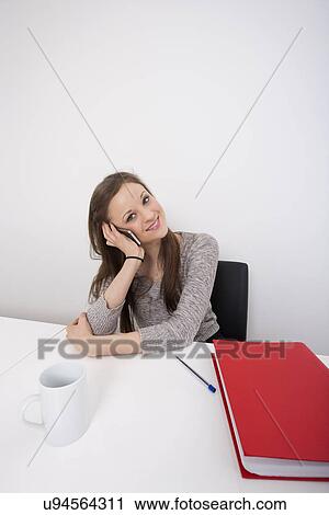 Stock Image - Portrait of beautiful businesswoman using cell phone at office desk. Fotosearch