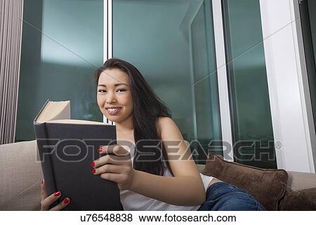 Portrait of beautiful young woman reading book in living room View Large Photo Image Stock Photo - Portrait of beautiful young woman reading book in living room. Fotosearch
