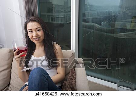 Portrait of beautiful young woman holding glass of red wine in living room View Large Photo Image Stock Photograph - Portrait of beautiful young woman holding glass of red wine in living room. Fotosearch