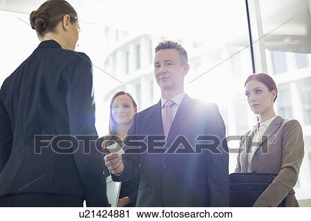 Stock Image - Portrait of businessman giving his card to businesswoman in office. Fotosearch