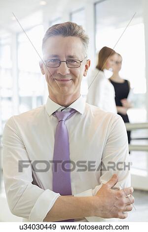 Stock Photo - Portrait of confident businessman standing arms crossed in office. Fotosearch