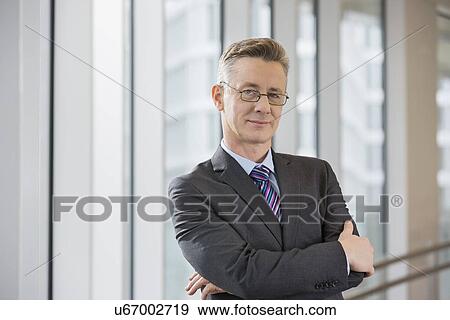 Stock Photo - Portrait of confident businessman standing arms crossed in office. Fotosearch