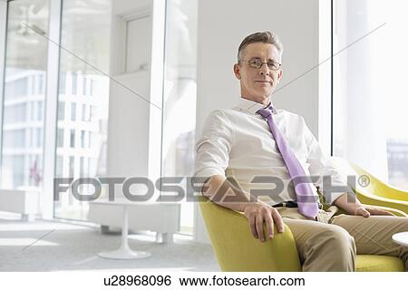 Stock Photograph - Portrait of confident businessman sitting at office lobby. Fotosearch