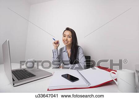 Stock Image - Portrait of confident businesswoman working in office. Fotosearch