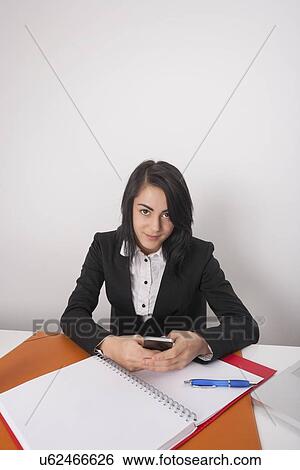 Portrait of confident businesswoman with cell phone sitting at office desk View Large Photo Image Stock Photograph - Portrait of confident businesswoman with cell phone sitting at office desk. Fotosearch