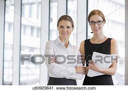 Stock Image - Portrait of confident businesswomen with documents in office. Fotosearch
