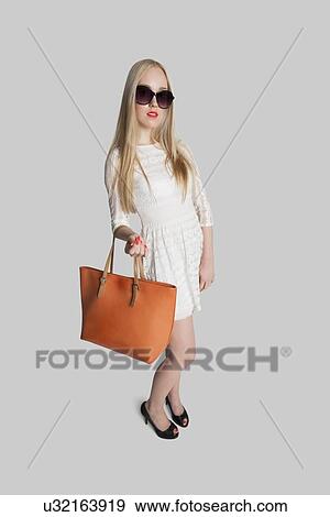 Stock Photo - Portrait of fashionable girl carrying purse over gray background. Fotosearch