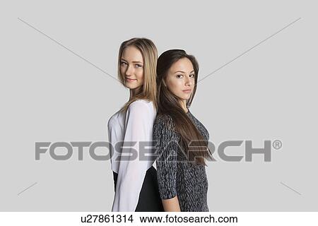 Portrait of female friends standing back to back over white background View Large Photo Image Picture - Portrait of female friends standing back to back over white background. Fotosearch