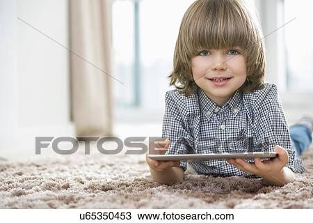 Portrait of happy boy with digital tablet lying on rug at home View Large Photo Image Stock Image - Portrait of happy boy with digital tablet lying on rug at home. Fotosearch