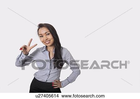 Picture - Portrait of happy businesswoman showing victory sign against gray background. Fotosearch