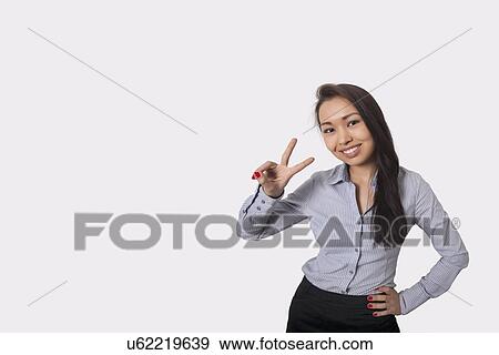 Portrait of happy businesswoman showing victory sign against gray background View Large Photo Image Stock Photo - Portrait of happy businesswoman showing victory sign against gray background. Fotosearch