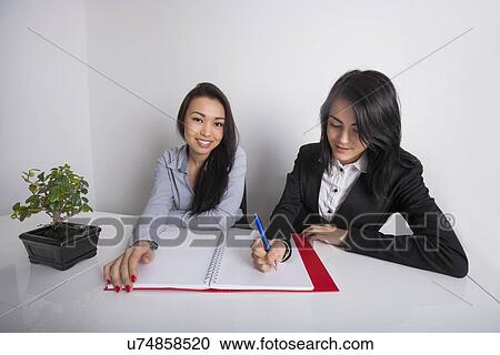 Portrait of happy businesswoman with colleague writing in spiral notebook at office desk View Large Photo Image Stock Image - Portrait of happy businesswoman with colleague writing in spiral notebook at office desk. Fotosearch