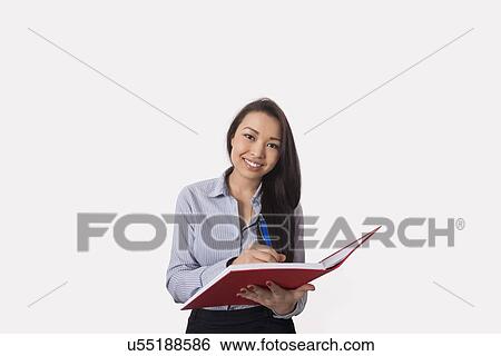 Stock Photograph - Portrait of happy businesswoman with book and pen over white background. Fotosearch