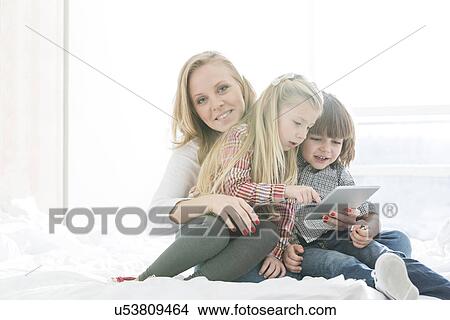 Portrait of happy mother with children using digital tablet in bedroom View Large Photo Image Picture - Portrait of happy mother with children using digital tablet in bedroom. Fotosearch