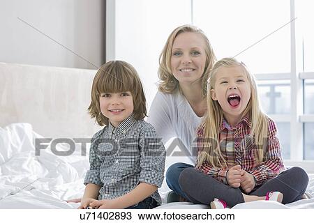 Stock Image - Portrait of happy mother with children in bedroom. Fotosearch
