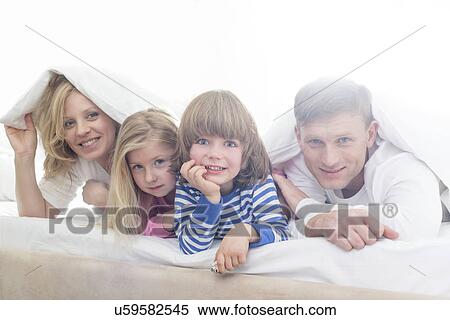 Stock Photography - Portrait of happy parents and children lying under bed cover. Fotosearch