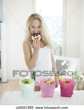 Portrait of happy woman eating cookie at kitchen counter View Large Photo Image Stock Image - Portrait of happy woman eating cookie at kitchen counter. Fotosearch
