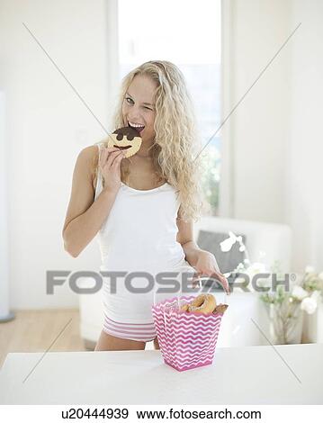 Portrait of happy woman eating cookie while winking at kitchen counter View Large Photo Image Stock Photo - Portrait of happy woman eating cookie while winking at kitchen counter. Fotosearch
