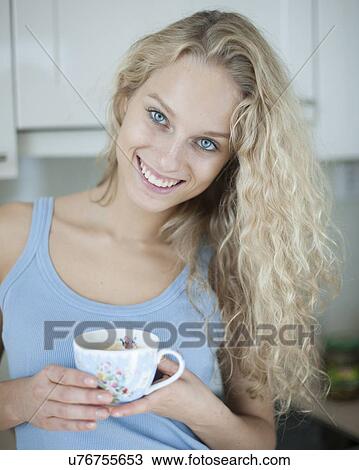 Stock Image - Portrait of happy woman holding tea cup in house. Fotosearch