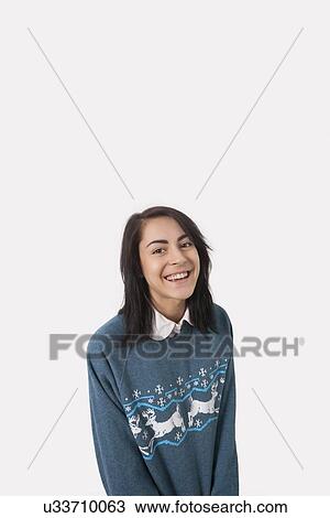 Stock Image - Portrait of happy woman in Christmas jumper against gray background. Fotosearch