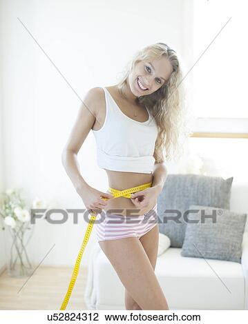 Stock Image - Portrait of happy woman measuring waist with tape. Fotosearch