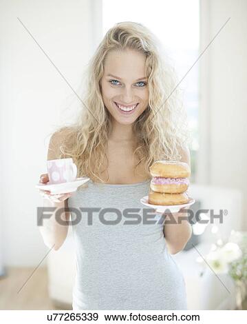 Stock Photo - Portrait of happy woman with tea and donut in house. Fotosearch