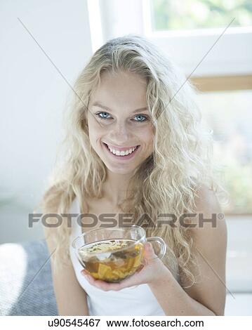 Portrait of happy young woman holding herbal tea cup in house View Large Photo Image Stock Photo - Portrait of happy young woman holding herbal tea cup in house. Fotosearch