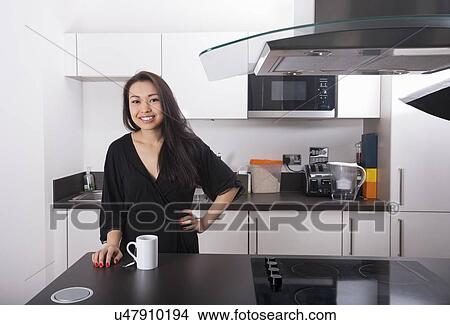 Picture - Portrait of happy young woman with coffee mug in kitchen. Fotosearch