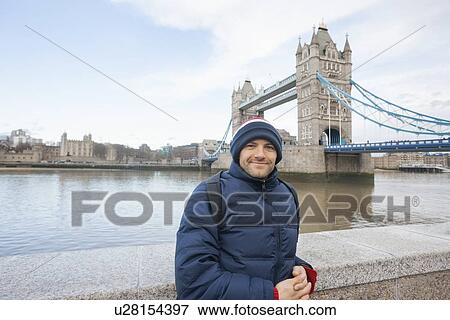 Stock Photo - Portrait of mid adult man in warm clothing standing in front of tower bridge, London, UK. Fotosearch