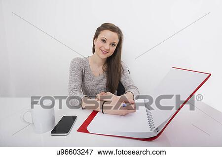 Stock Photo - Portrait of smiling businesswoman writing notes at desk in office. Fotosearch