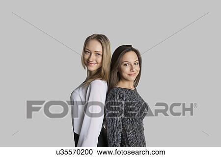 Stock Image - Portrait of smiling friends standing back to back against gray background. Fotosearch