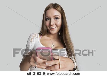 Stock Photo - Portrait of smiling woman with cell phone against gray background. Fotosearch