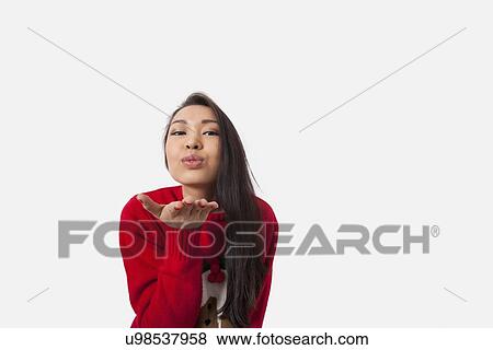 Stock Photo - Portrait of woman in Christmas sweater blowing kiss over gray background. Fotosearch