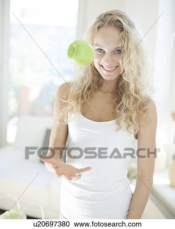 Portrait of young woman catching apple in kitchen View Large Photo Image Stock Image - Portrait of young woman catching apple in kitchen. Fotosearch