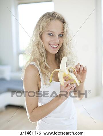 Stock Photography - Portrait of young woman peeling banana in house. Fotosearch