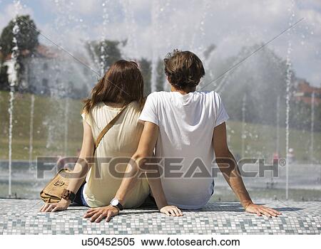 Stock Photography - Rear view of couple sitting on fountain wall. Fotosearch
