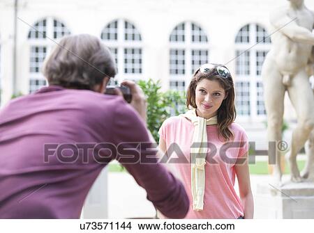 Picture - Rear view of man photographing woman against building. Fotosearch