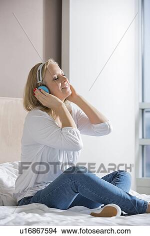 Picture - Relaxed mid adult woman enjoying music on headphones in bedroom. Fotosearch