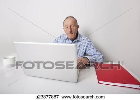Senior businessman using laptop at office desk View Large Photo Image Stock Photo - Senior businessman using laptop at office desk. Fotosearch