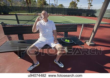 Senior male tennis player drinking water while relaxing on court View Large Photo Image Stock Image - Senior male tennis player drinking water while relaxing on court. Fotosearch