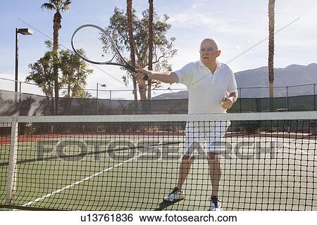 Stock Photograph - Senior male tennis player preparing to serve on court. Fotosearch