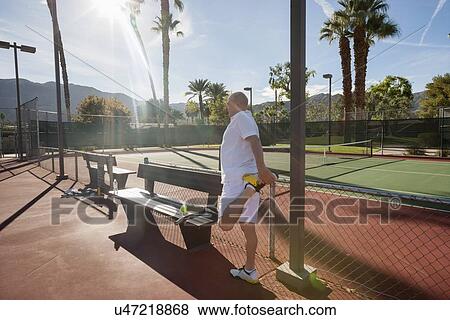 Stock Photo - Senior male tennis player stretching leg on court. Fotosearch