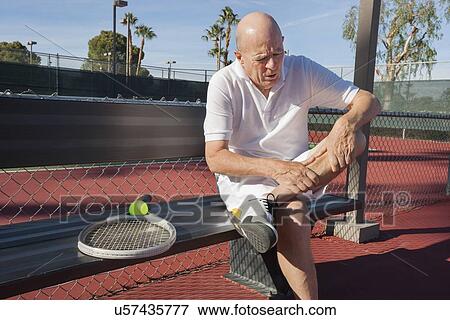 Senior male tennis player with leg pain sitting on bench at court View Large Photo Image Stock Photo - Senior male tennis player with leg pain sitting on bench at court. Fotosearch