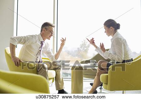 Stock Photo - Side view of business people conversing at lobby. Fotosearch