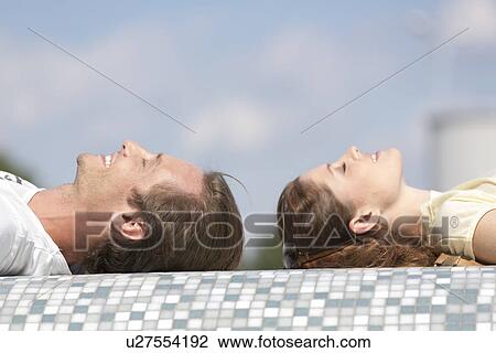 Stock Image - Side view of couple relaxing on mosaic wall. Fotosearch