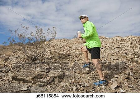 Side view of senior man holding water bottle while standing on mountain View Large Photo Image Picture - Side view of senior man holding water bottle while standing on mountain. Fotosearch