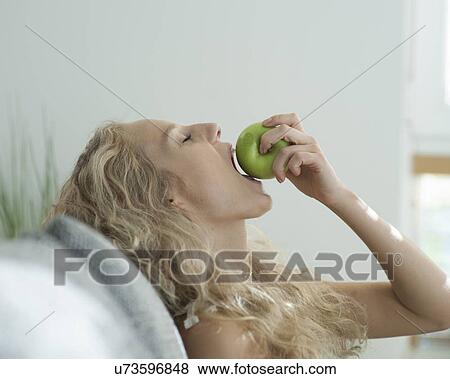 Stock Photo - Side view of sensuous woman biting apple in house. Fotosearch
