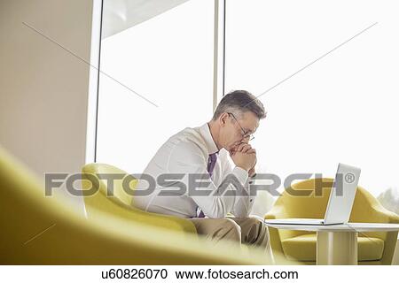 Side view of serious businessman looking at laptop in lobby View Large Photo Image Stock Image - Side view of serious businessman looking at laptop in lobby. Fotosearch